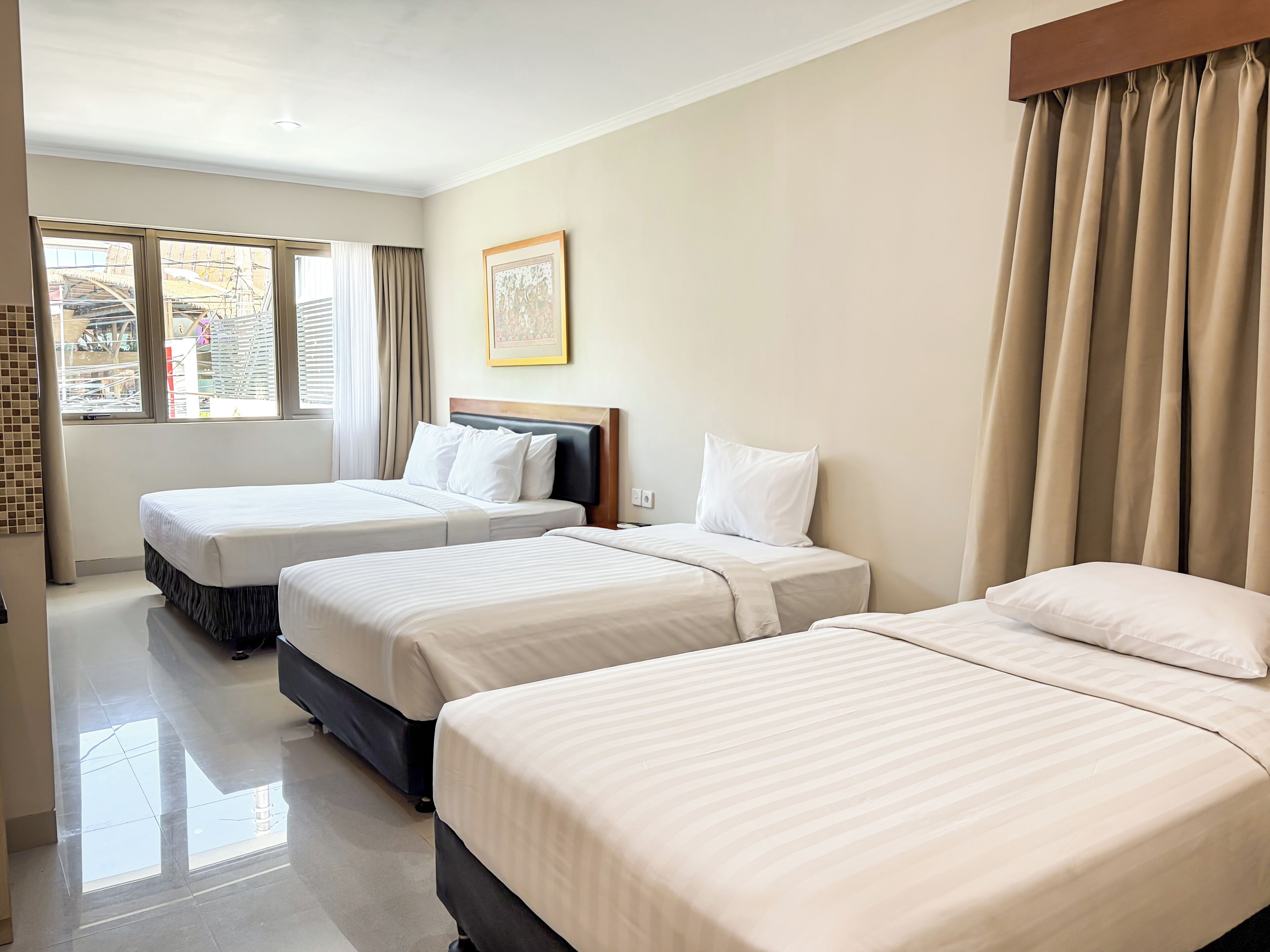 Habitación de hotel con tres camas, un ventanal con cortinas, un cuadro enmarcado en la pared y piso de baldosas.