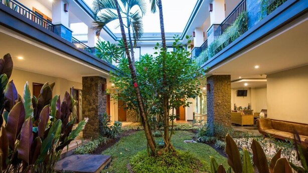 A hotel lobby with a central garden, stone pillars, and a glass ceiling. - Svarna Hotel Sanur (Denpasar)