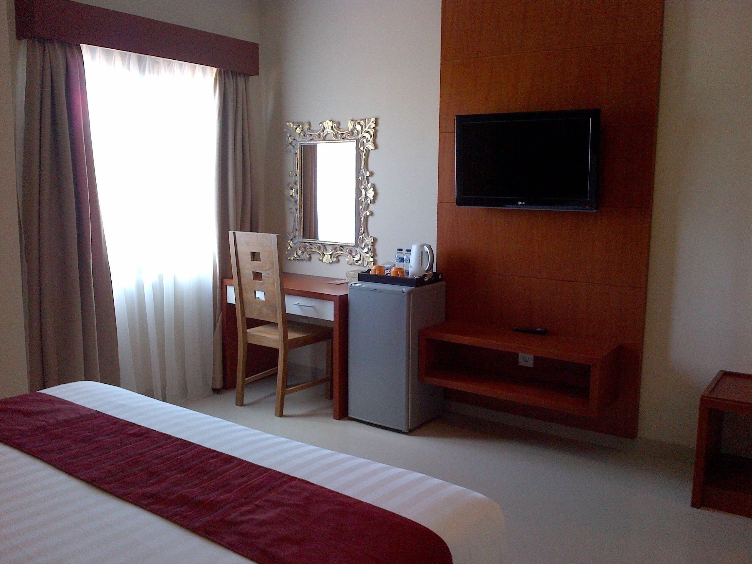A hotel room with a bed, a desk, a chair, a television, and a small refrigerator.