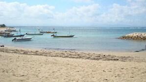 A beach with several boats anchored in calm waters, a sandy shore, and a clear sky. - Svarna Hotel Sanur (Denpasar)
