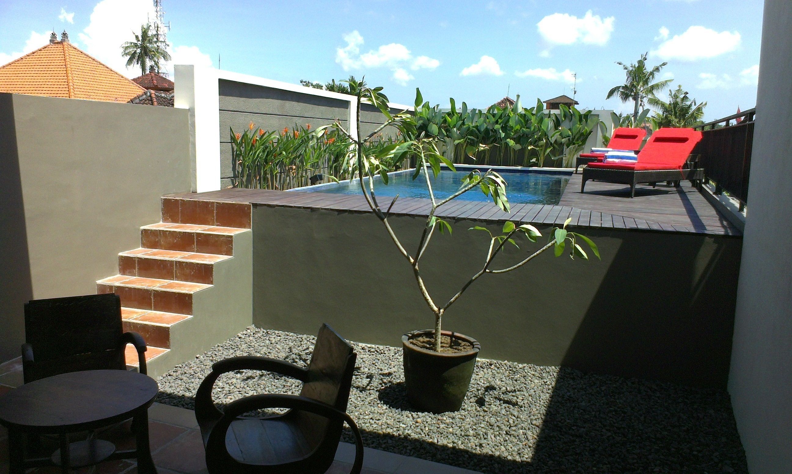 A pool area with a small garden, a wooden deck, and a seating area with chairs and a table.