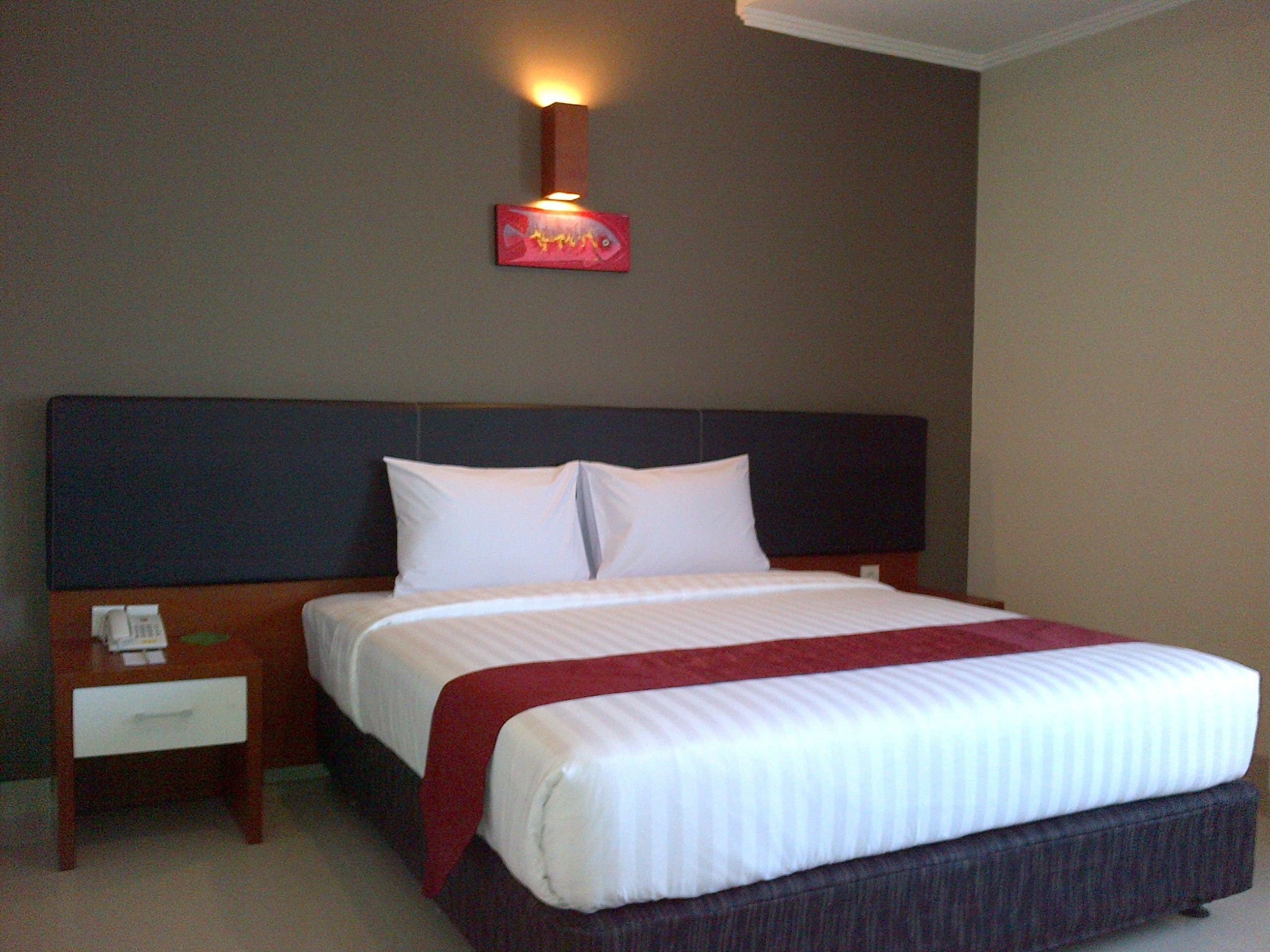 A hotel room with a large bed, a nightstand, and a wall-mounted light fixture.