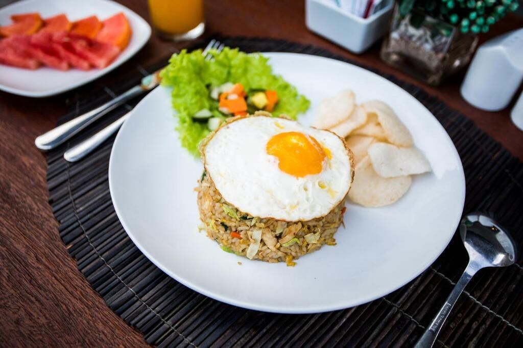 A plate of fried rice with a fried egg on top, accompanied by a side salad and potato chips.