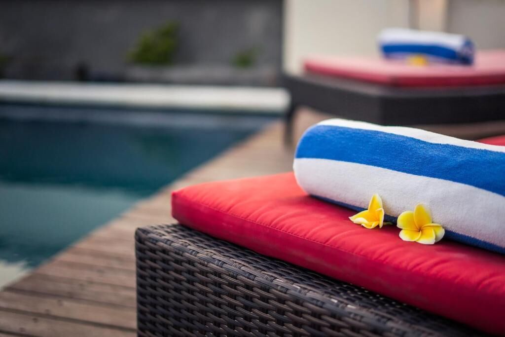 A poolside area with wicker furniture and a red cushion with a blue and white towel.