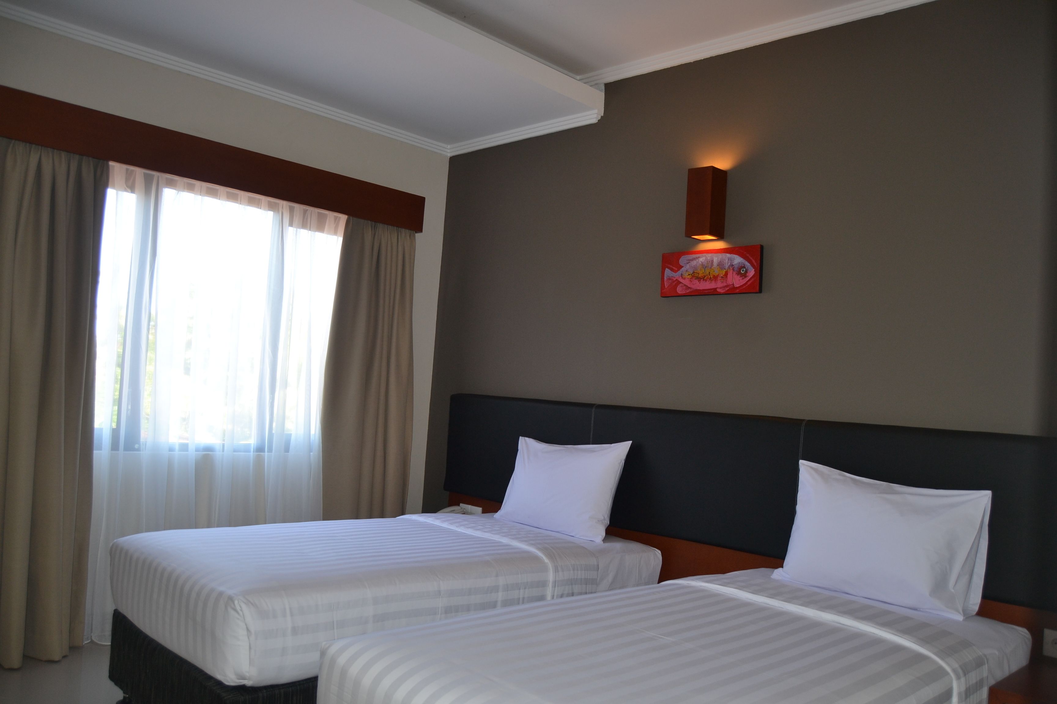A hotel room with two beds, a nightstand, a wall-mounted lamp, and a window with curtains.