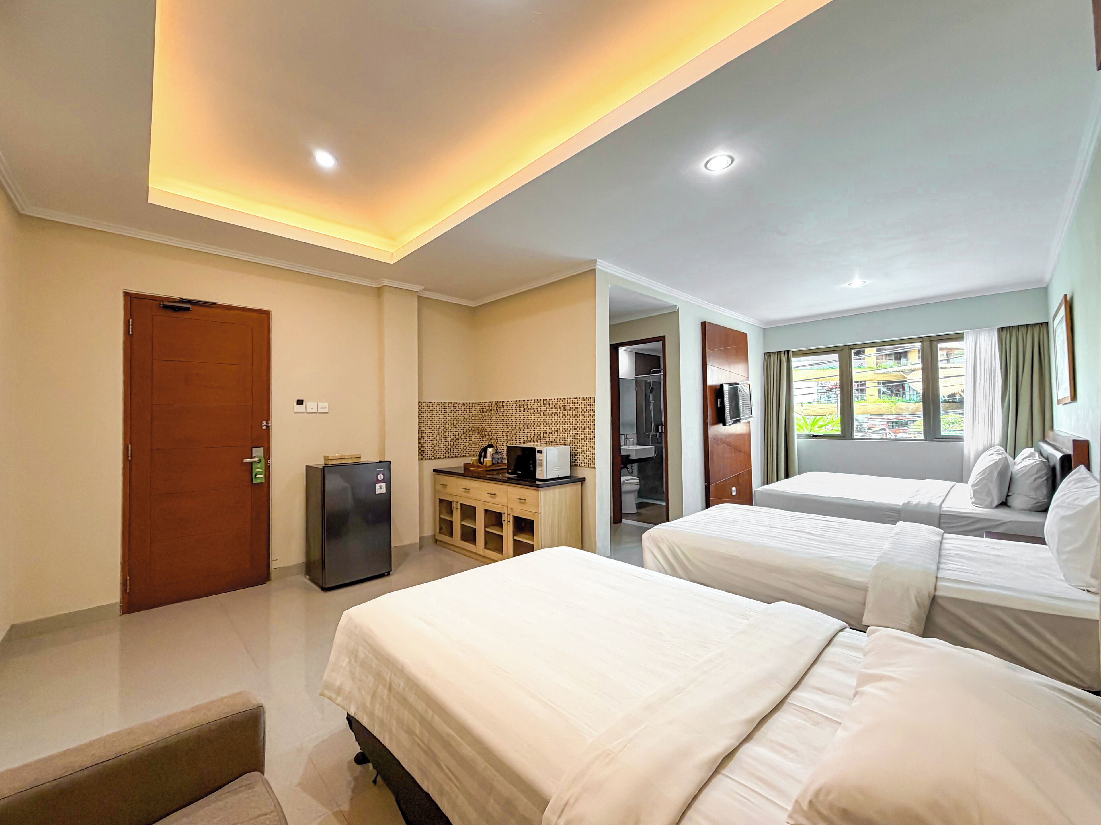 A hotel room with two beds, a kitchenette, a bathroom, and a view of the outside.