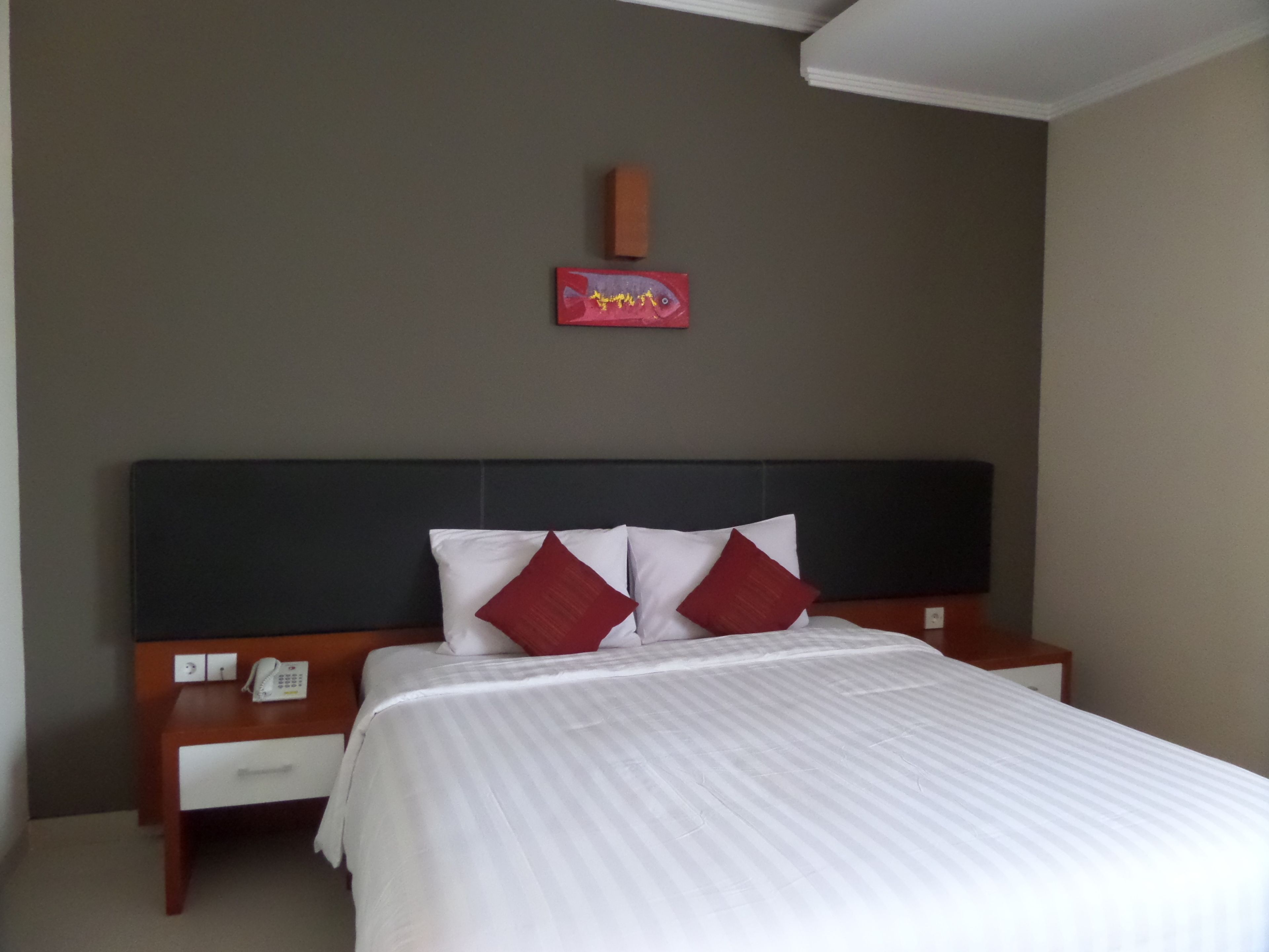 A hotel room with a bed, a nightstand, a telephone, and a wall-mounted artwork.