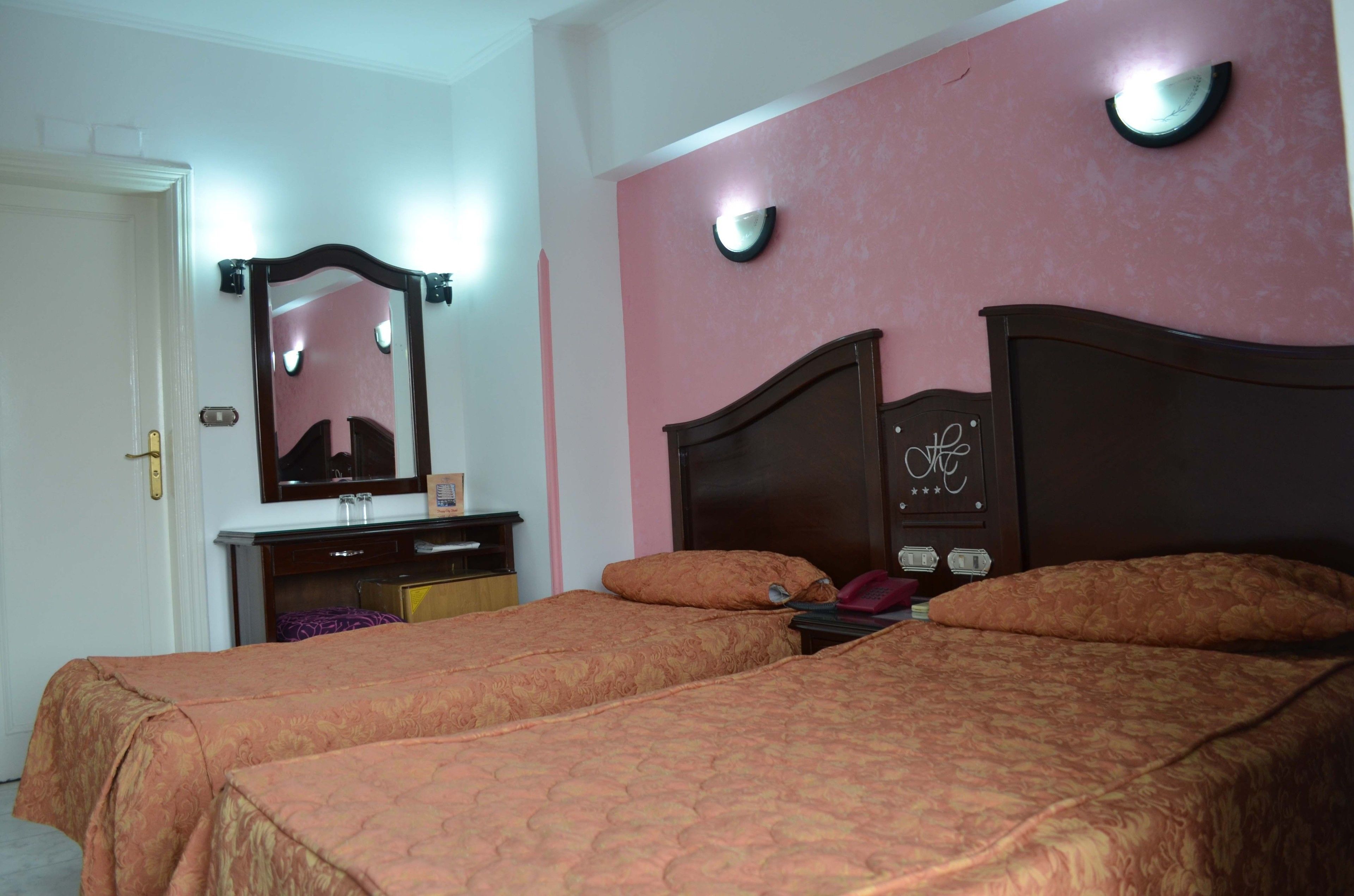 Ein Hotelzimmer mit zwei Betten, einem Schminktisch, einem Spiegel und einer Wanduhr.