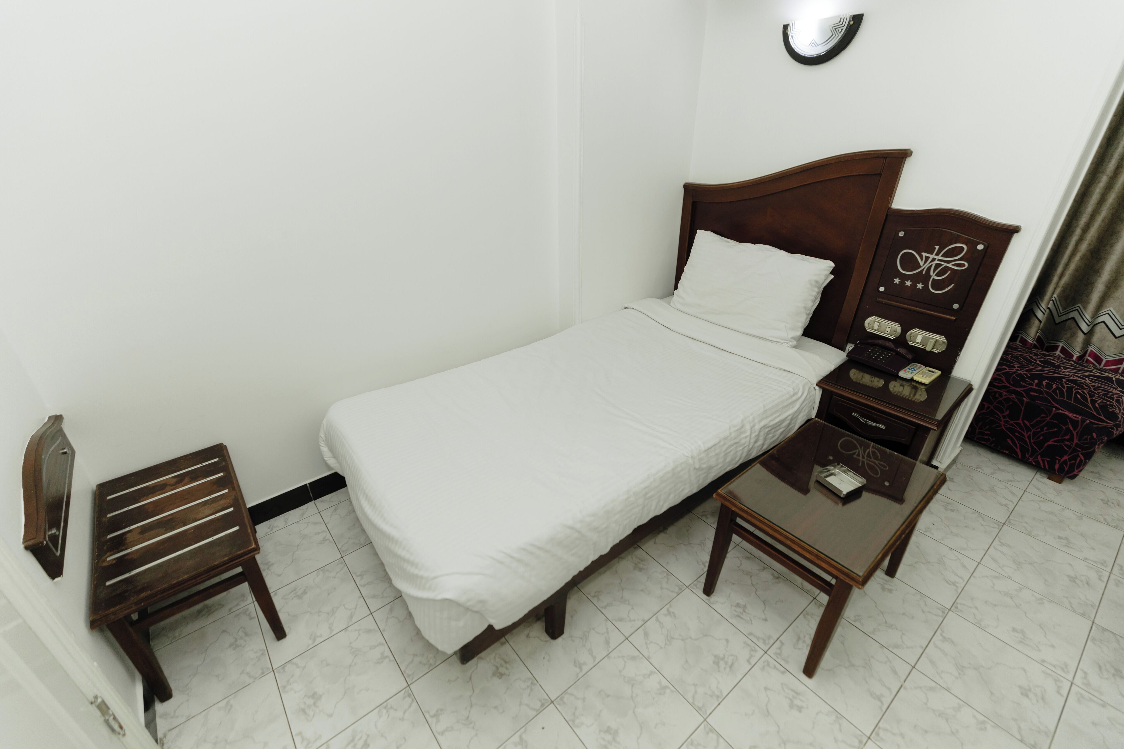 Une chambre d’hôtel bien rangée, avec un lit simple, une petite table, une table de chevet et un téléphone fixé au mur.