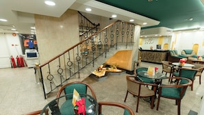 Un vestíbulo de hotel con una escalera de mármol, sillas tapizadas en verde y un mostrador de recepción.
