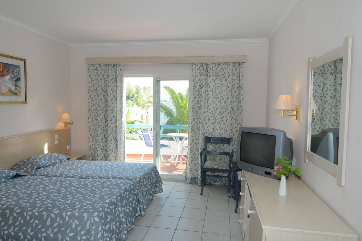 A hotel room with two beds, a television, a small table, and a window with curtains.