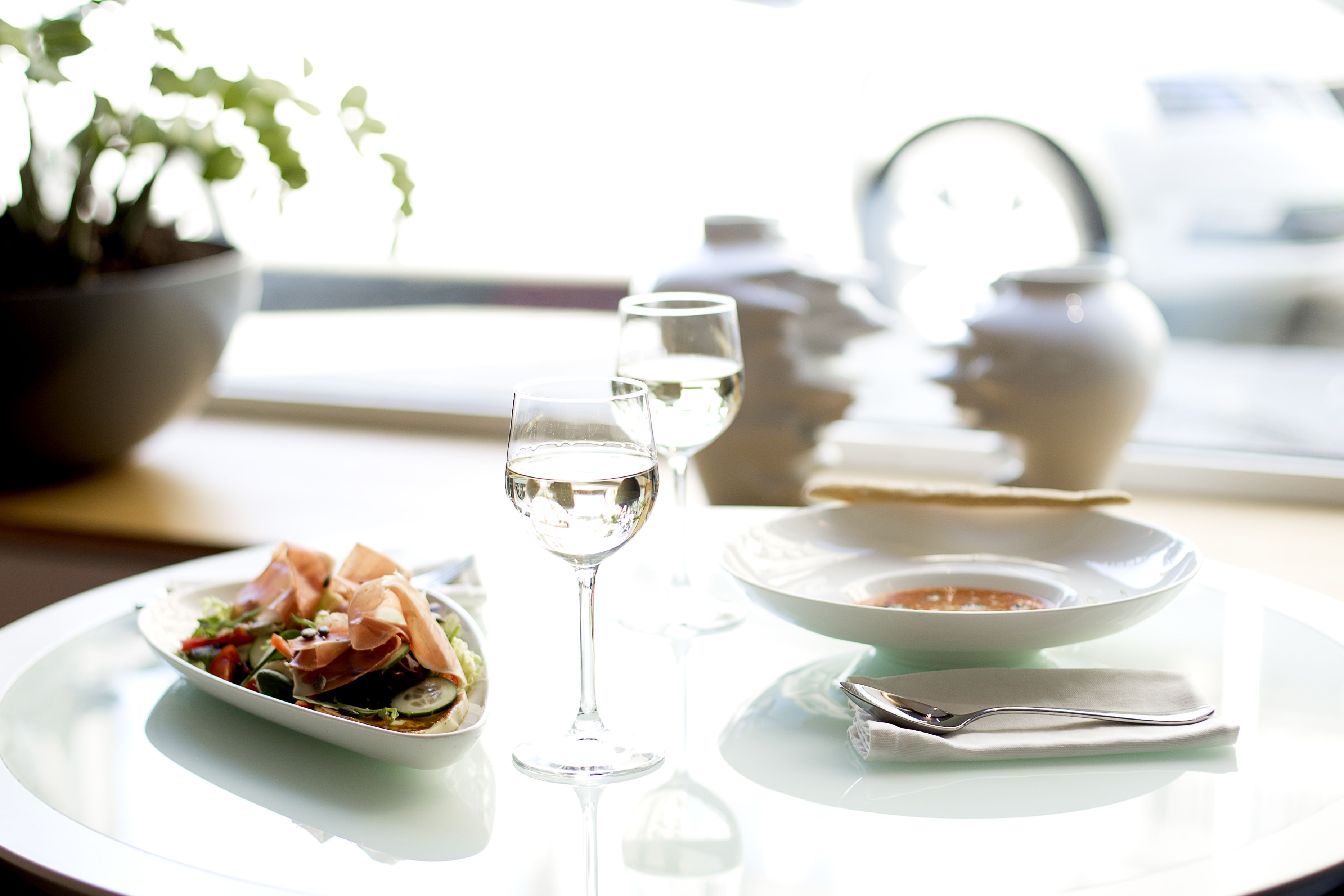 Una mesa de comedor con ensalada, dos copas de vino, un tazón de sopa y una cuchara.