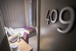 Quarto de hotel moderno com uma cama, uma escrivaninha com um laptop, um vaso com flores e o número do quarto visível, 409.
