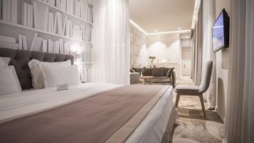 A modern hotel room with a large bed, a bookshelf, a seating area, and a TV mounted on the wall.