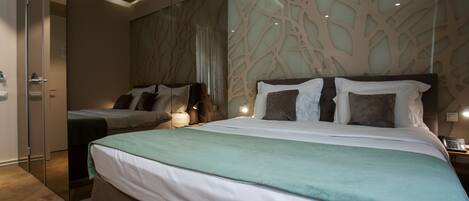 A modern hotel room with a large bed, a smaller bed, and a glass partition.