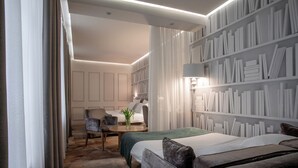 Una camera d'albergo moderna con un letto grande, una poltrona, una scrivania e una libreria piena di libri.