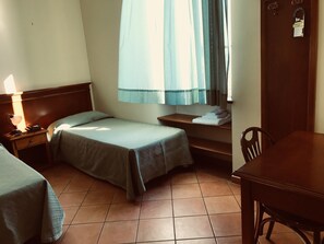 A small, clean room with two single beds, a wooden nightstand with a lamp, a small table, and a chair. - Villino Gregoraci Relais (Santa Marinella)