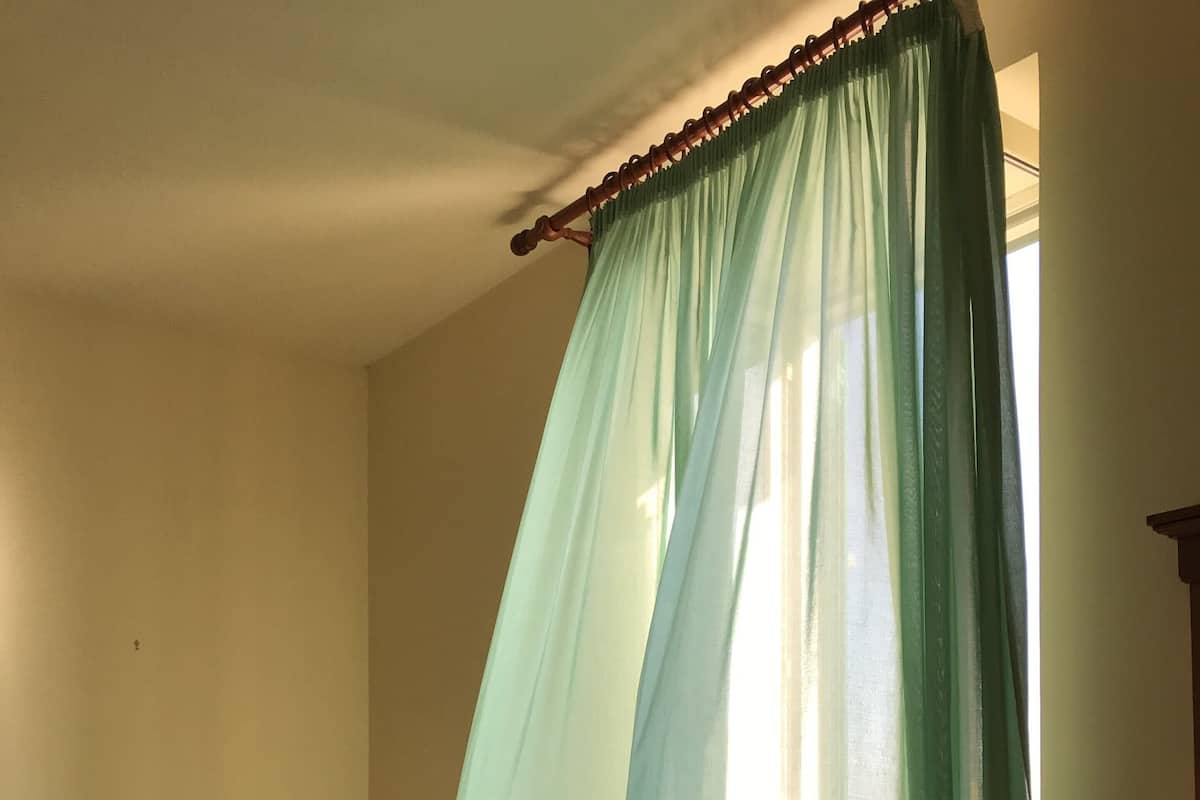 A small, single-bed room with a wooden headboard, a bedside table, and a window with a green curtain.