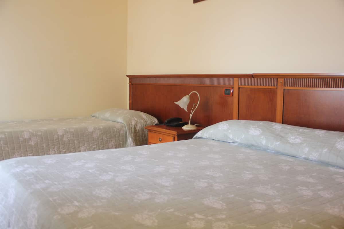 A hotel room with two single beds, a wooden headboard, a bedside table with a lamp, and a telephone.