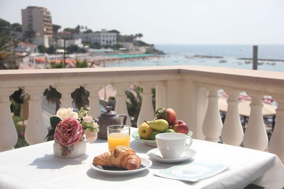 A balcony table with breakfast items, a vase with flowers, and a view of the beach and ocean.