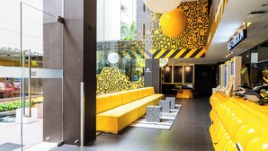 A modern lobby with a yellow sofa, a self-checkin station, and a glass wall offering a view of the outside. - Mood Hotel Pattaya (Pattaya)
