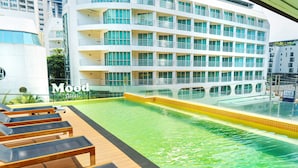 A pool area with lounge chairs and a hotel building in the background. - Mood Hotel Pattaya (Pattaya)