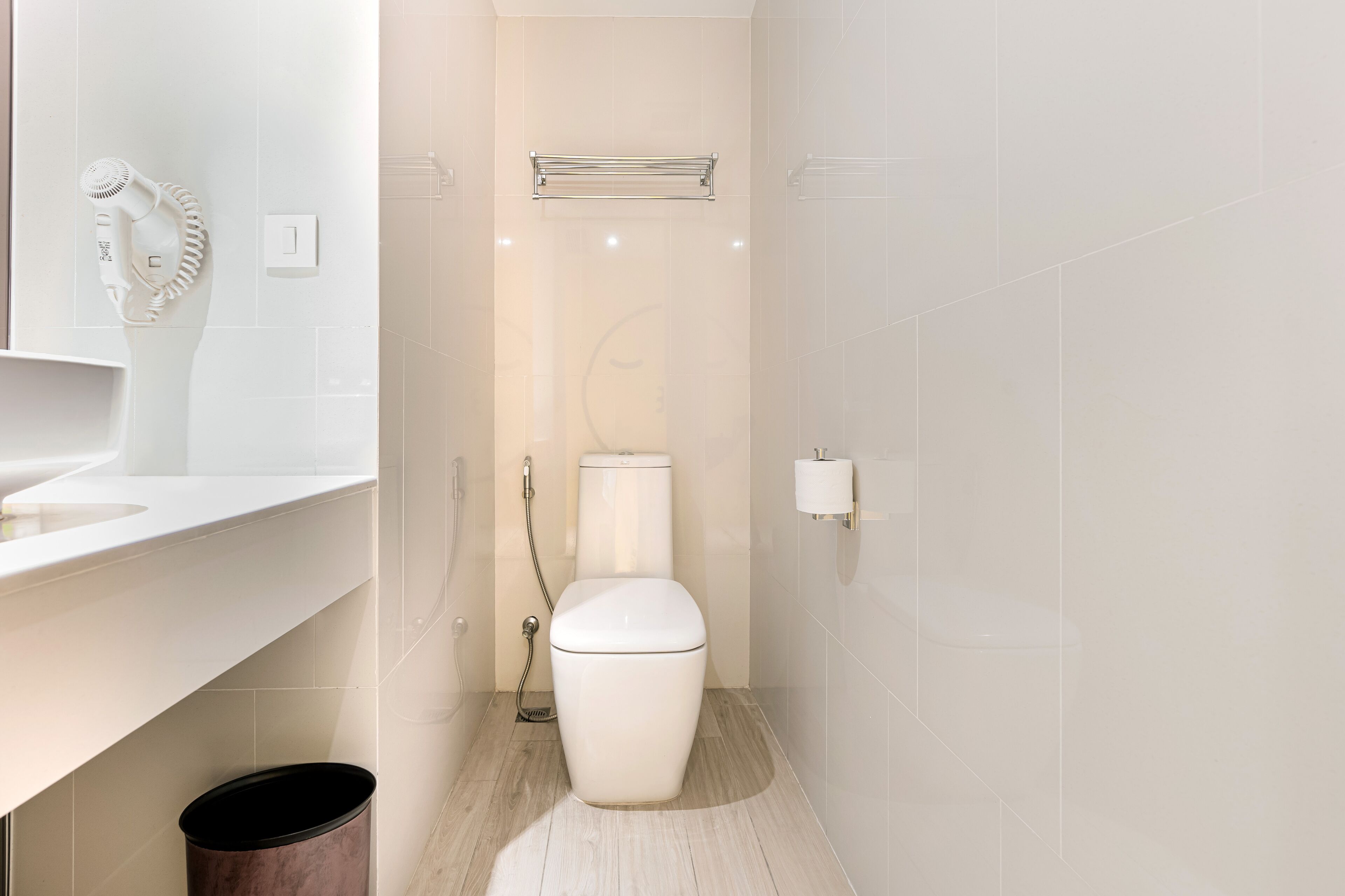 A modern bathroom with a toilet, a hand dryer, a towel rack, and a trash bin.