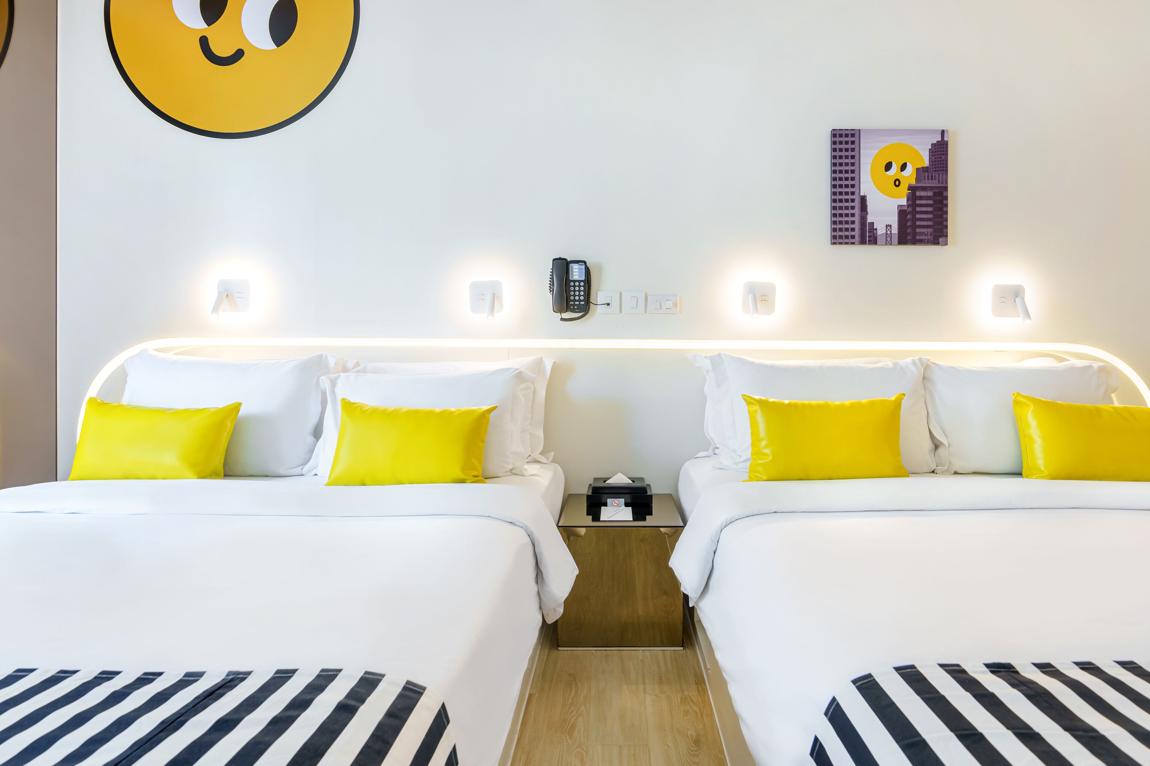 A hotel room with two beds, each with white bedding and yellow pillows, a bedside phone, and a small table between the beds.
