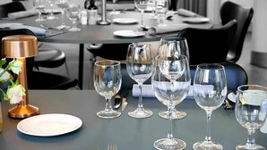 Une table à manger dressée avec des verres à vin, des assiettes et des couverts, agrémentée d’une lampe et d’un vase de fleurs.