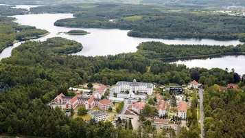 Vista aérea de un pueblo junto al lago, con un complejo edilicio destacado con edificios de techo rojo, rodeado de bosques densos y varios lagos.