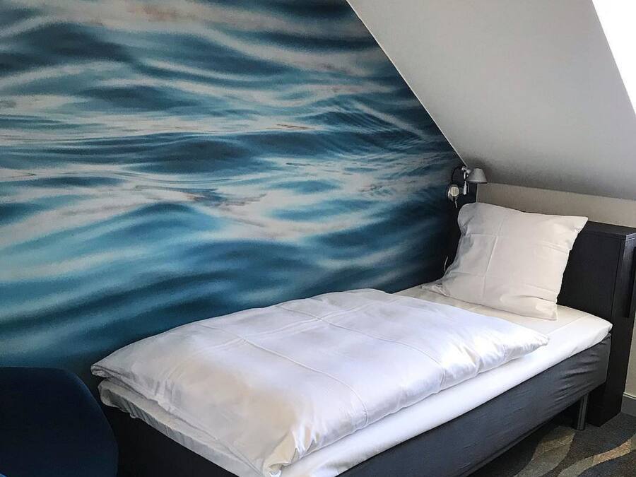 A small, modern room with a bed, a chair, and a wall mural.