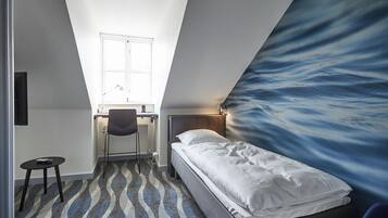 A small, modern room with a bed, a desk, and a chair.