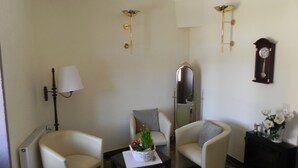 Una habitación con dos sillones, una mesa con una planta, una lámpara de pie, un espejo y un reloj en la pared.