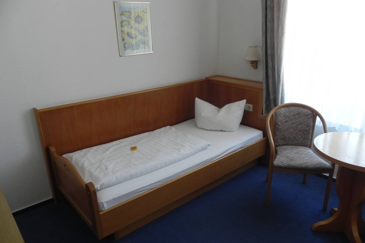 A single bed with a wooden headboard, a white pillow, and a small bedside table with a lamp.