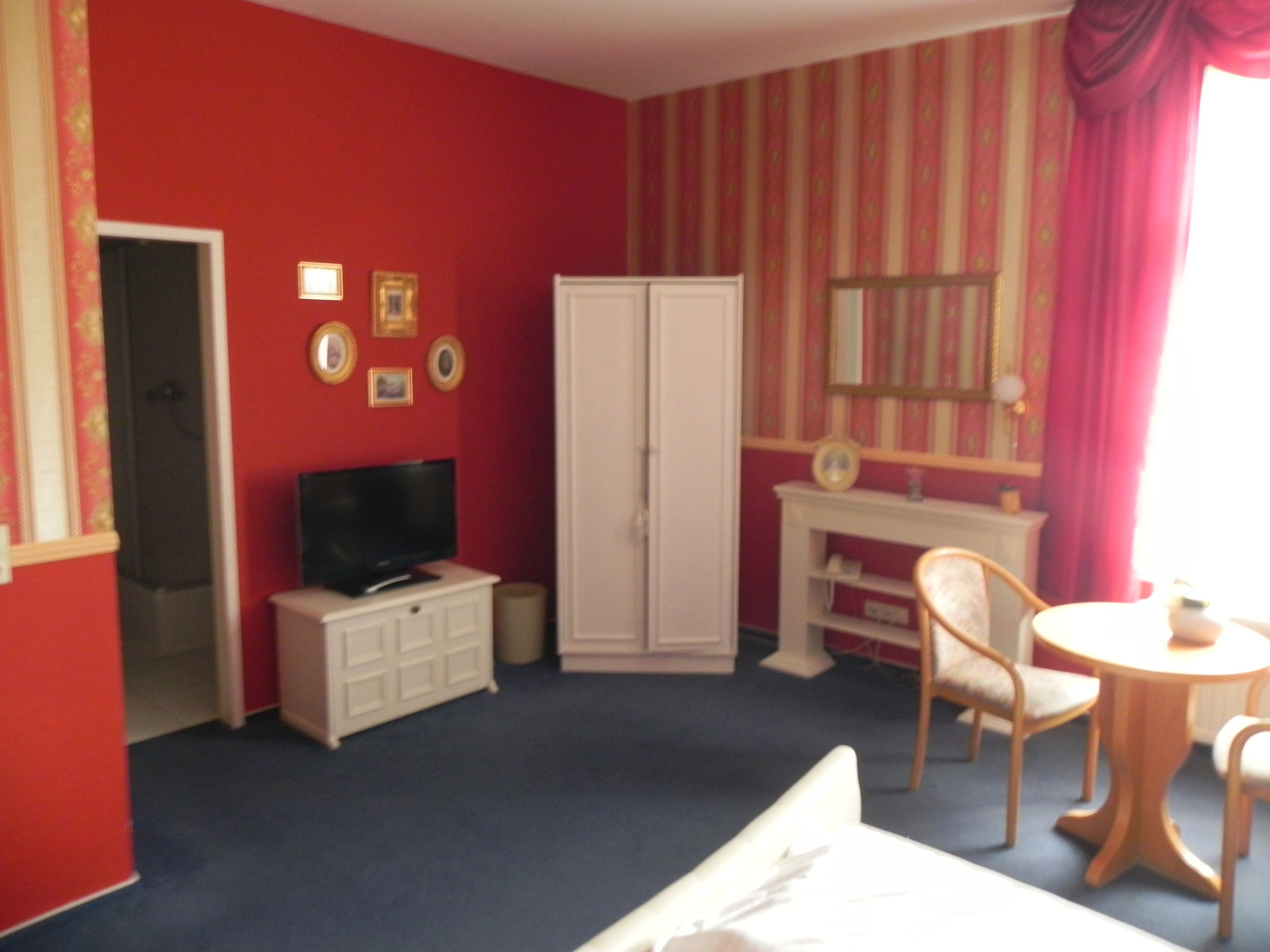 Ein Zimmer mit Fernseher, Kleiderschrank, Schreibtisch, Stuhl und kleinem Tisch.