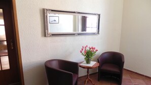 Una habitación con dos sillones oscuros, una mesita con un jarrón de flores y un espejo en la pared.