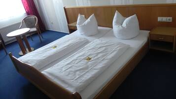 A neatly made bed with white linens and pillows, a wooden headboard, a bedside table, and a chair.