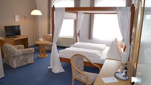 Una habitación de hotel con una cama, televisión, escritorio, silla y lámpara.