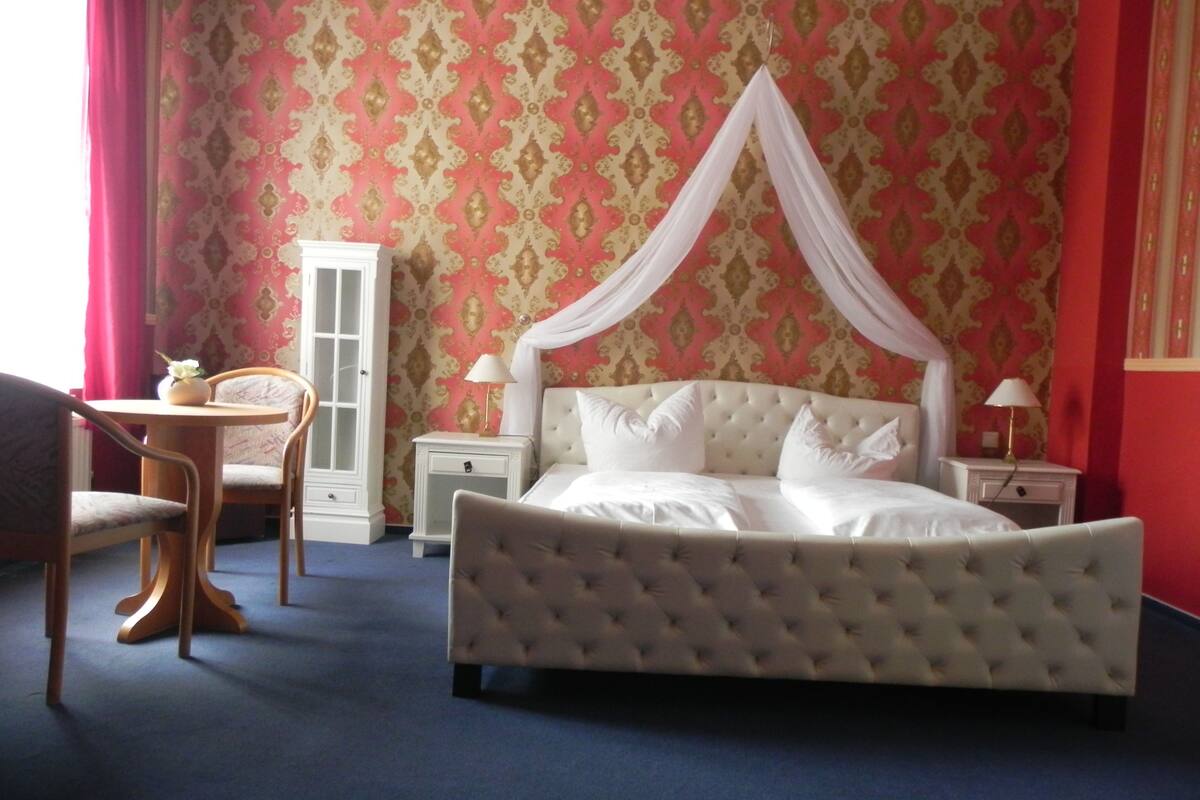 A bedroom with a large bed, a bedside table, a chair, and a wardrobe.