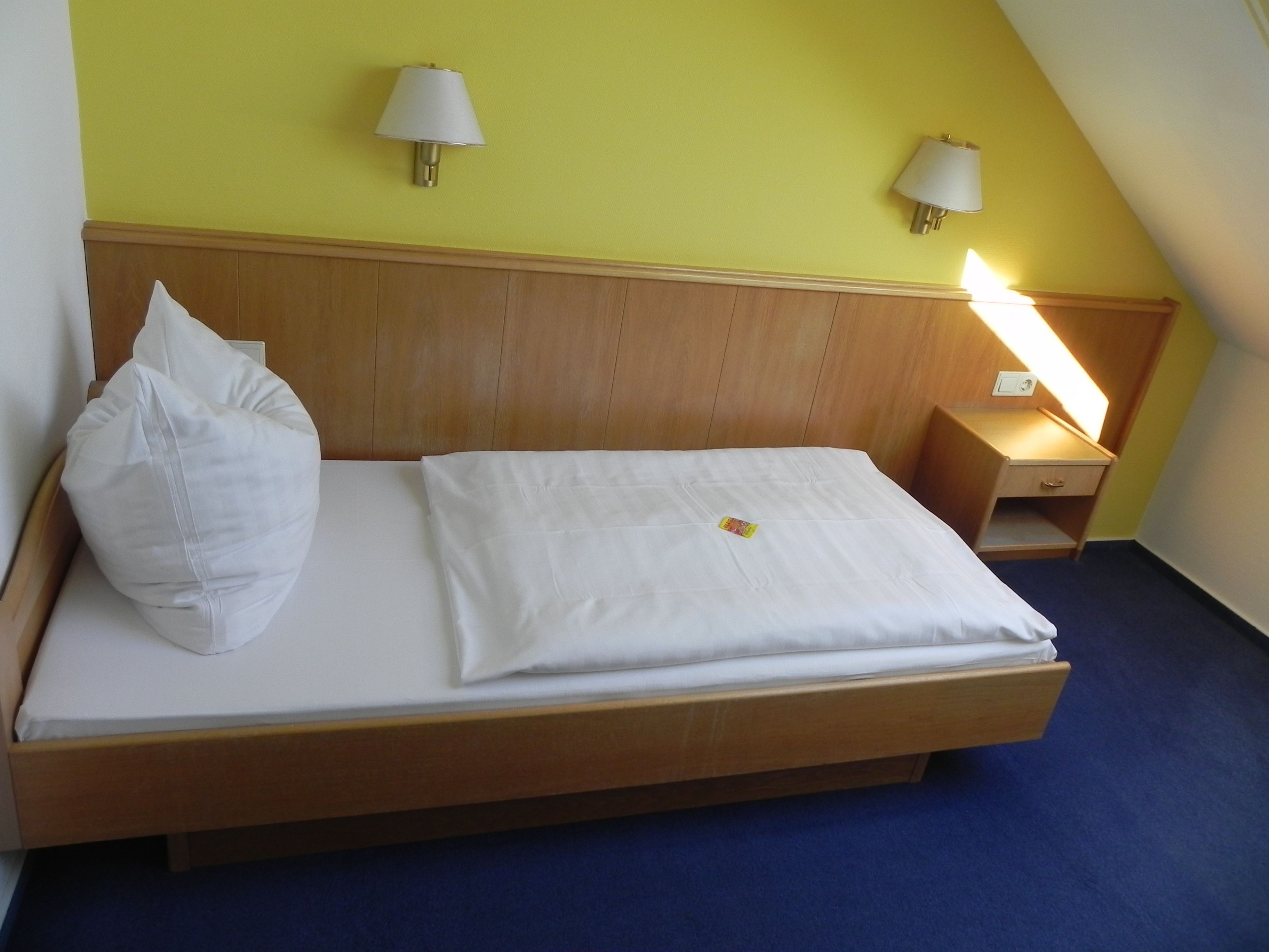 A neatly made bed with white linens, two wall-mounted lamps, and a bedside table with a lamp.