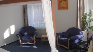 Una habitación de hotel con una cama, dos sillones, una mesita y una ventana con cortinas.