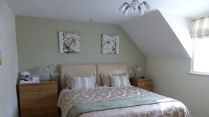 Un dormitorio con una cama grande, dos mesitas de noche, un ventilador de techo y dos cuadros florales colgados en la pared.