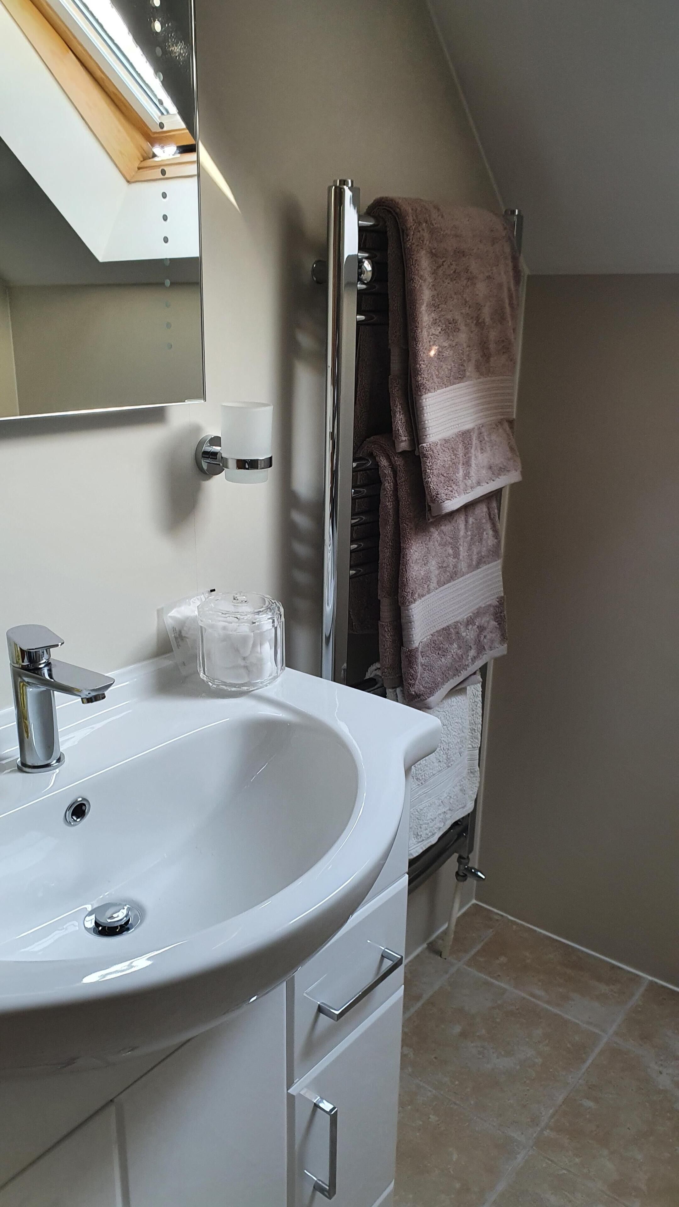 A bathroom with a white sink, a mirror, a towel rack with a brown towel, and a glass container on the counter.