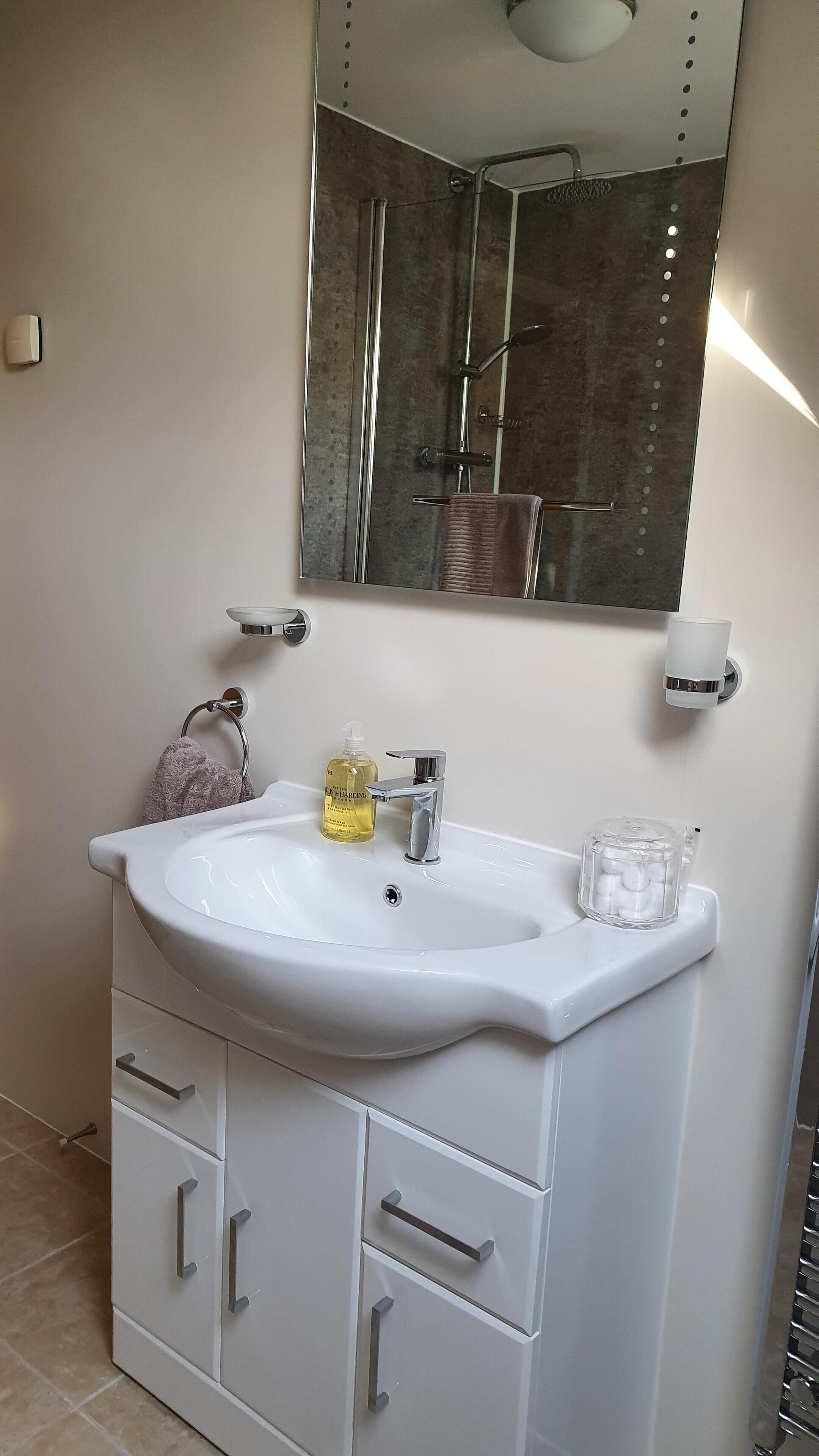 A bathroom with a white sink, a mirror, a towel rack, a soap dispenser, and a glass container.