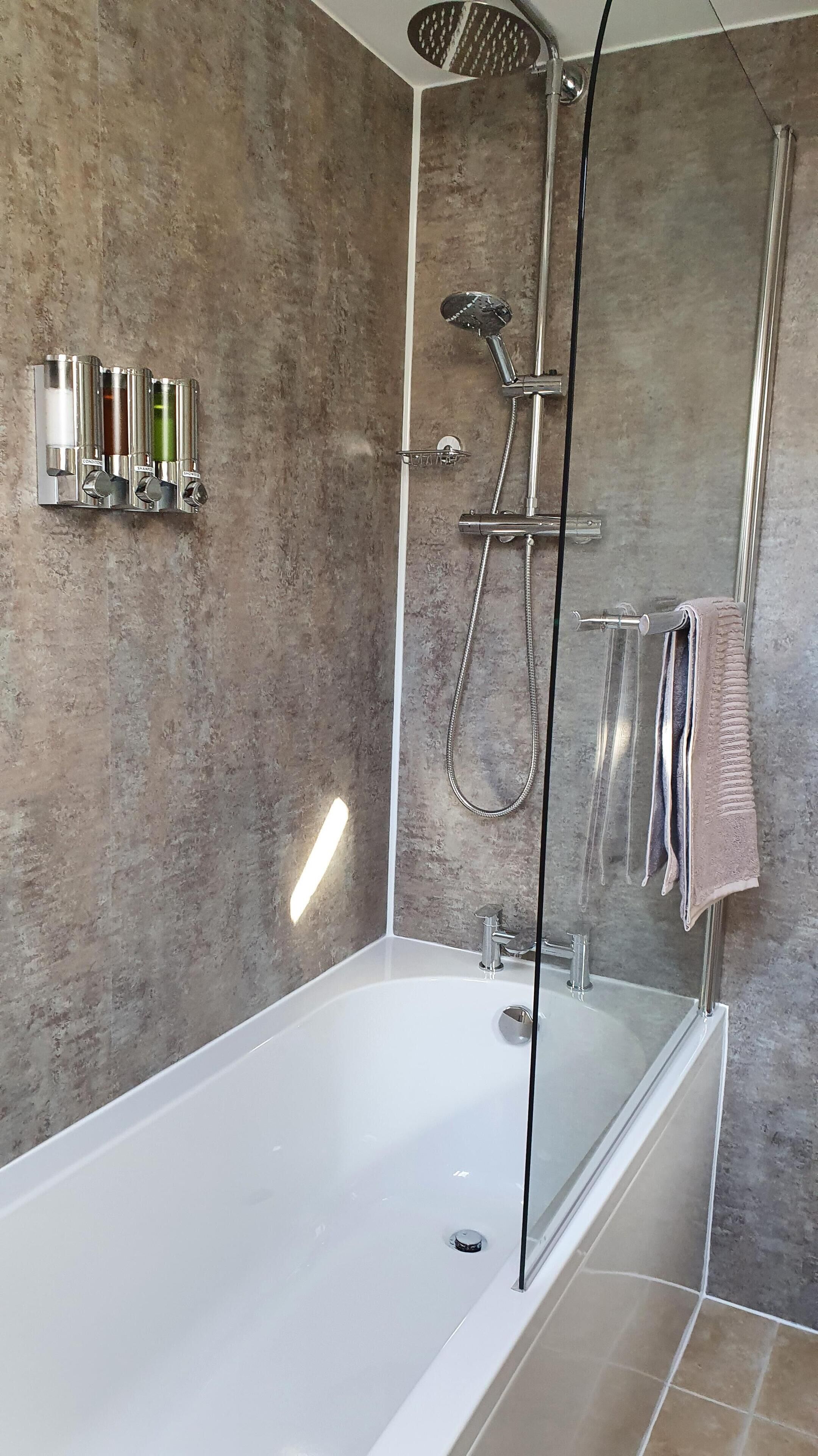 A modern bathroom with a glass-enclosed shower, a white bathtub, and a wall-mounted faucet.