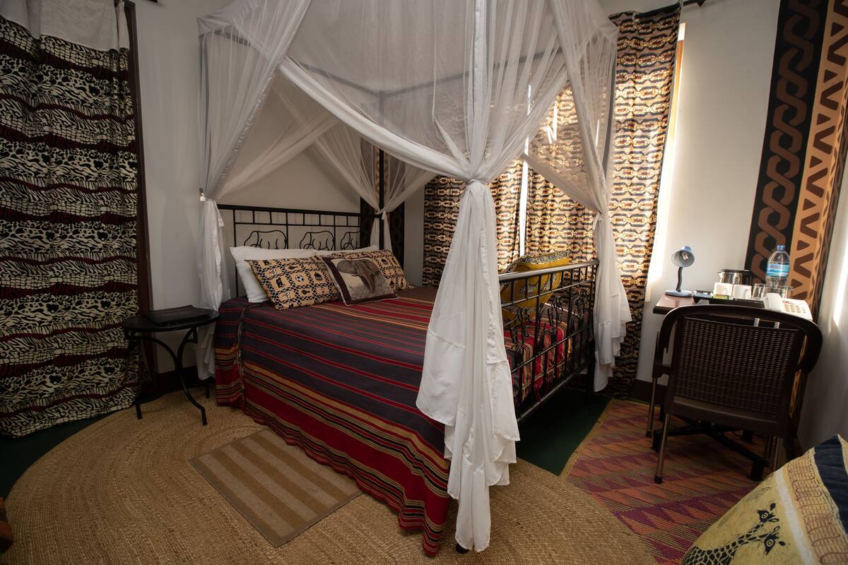 A room with a bed, a desk, a chair, and a window with curtains.