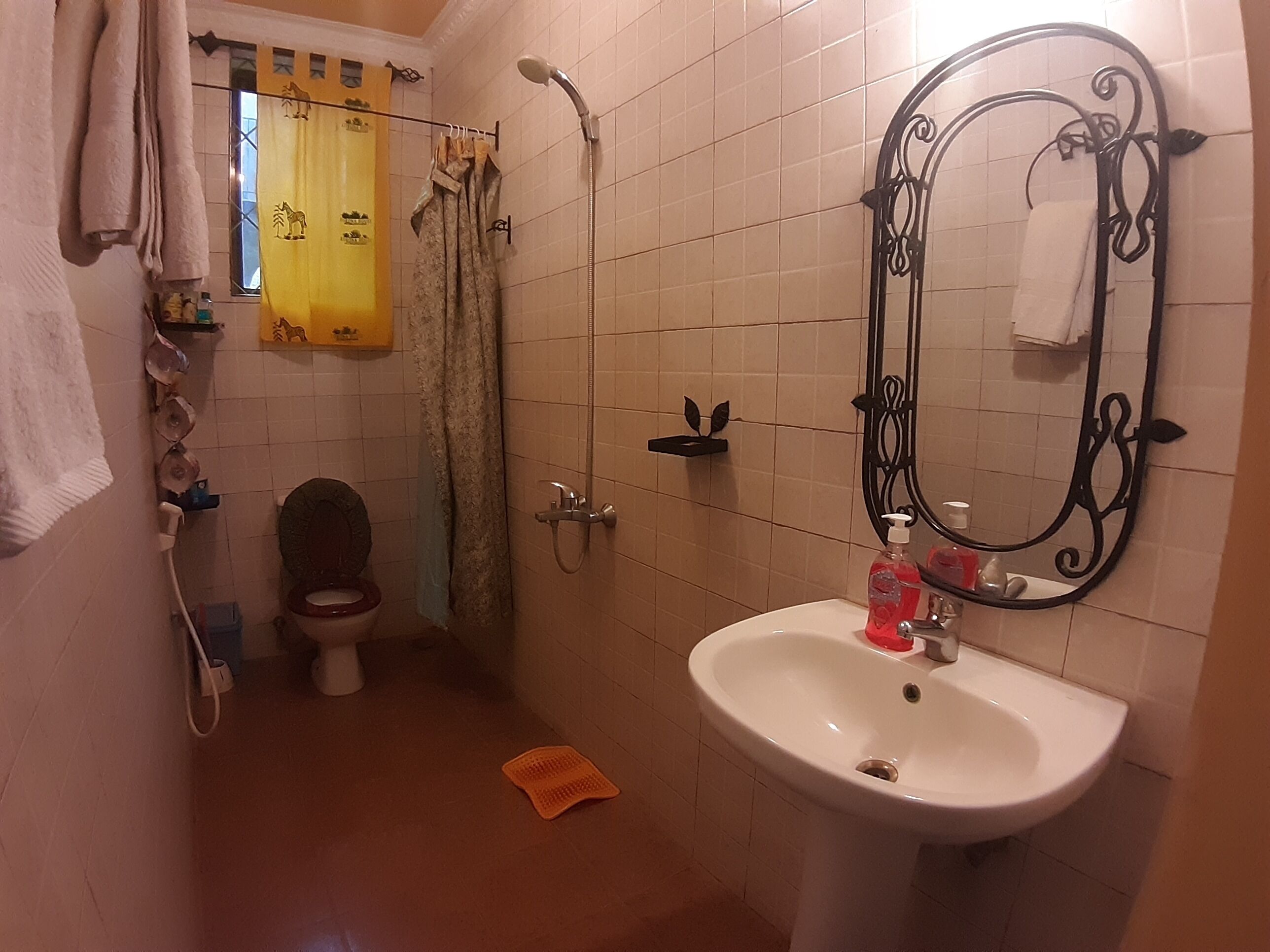 A bathroom with a toilet, shower, sink, and a mirror with a decorative frame.