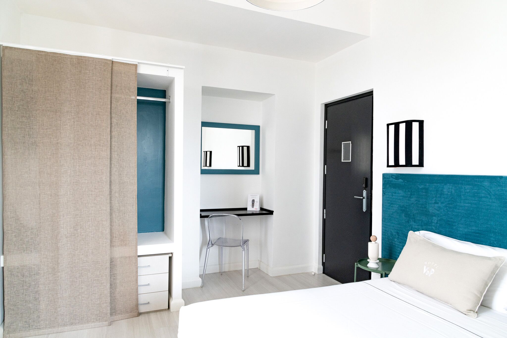 A modern hotel room with a bed, a desk, a chair, a wardrobe, and a door.