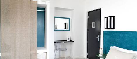 A modern hotel room with a bed, a desk, a chair, a wardrobe, and a door.