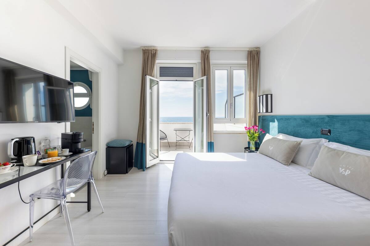 A hotel room with a bed, a desk with a chair, a TV, and a view of the outdoors.